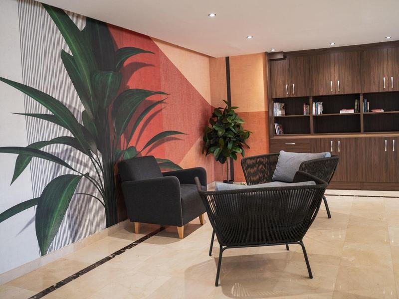 Moderní hotelová hala s černými křesly, dřevěnými policemi a velkou rostlinnou nástěnnou dekorací.