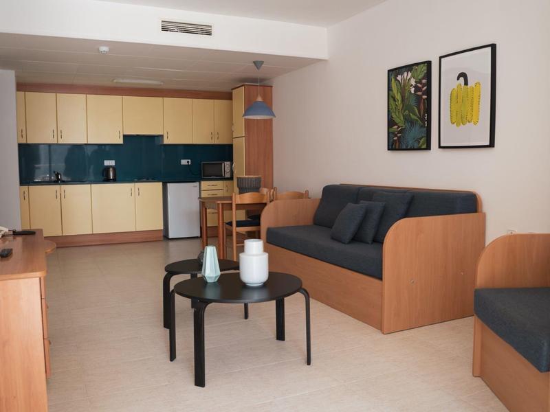 Moderní obývací pokoj s kuchyňským koutem, pohovkou a konferenčním stolkem v světlých barvách.