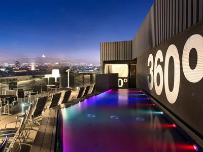 Moderne Dachterrasse mit beleuchtetem Pool, Lounge-Stühlen und Blick auf die Stadt bei Nacht.