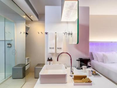 Moderne hotelkamer met witte wastafel, douche en bed met paarse verlichting.