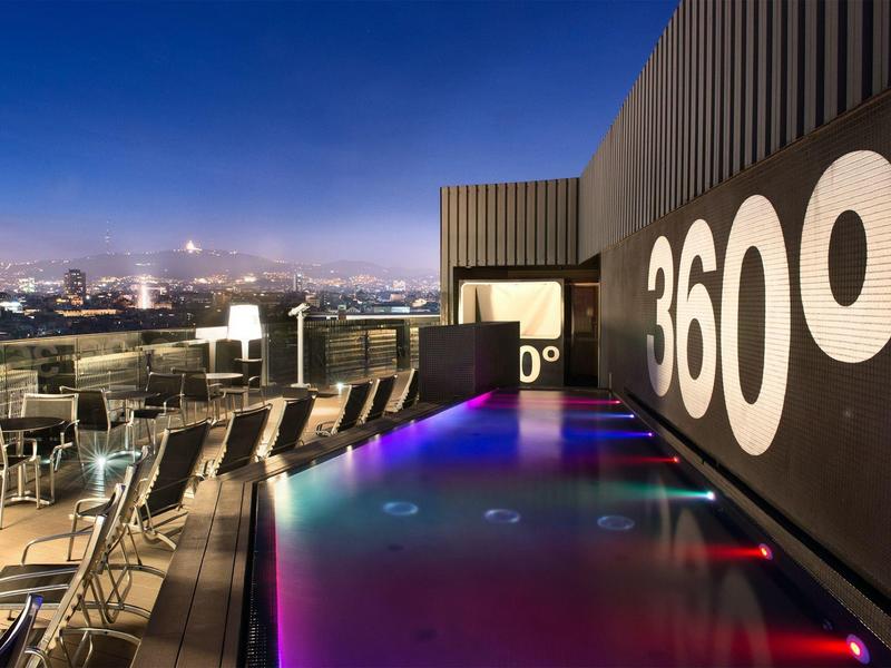Moderne Dachterrasse mit beleuchtetem Pool, Lounge-Stühlen und Blick auf die Stadt bei Nacht.