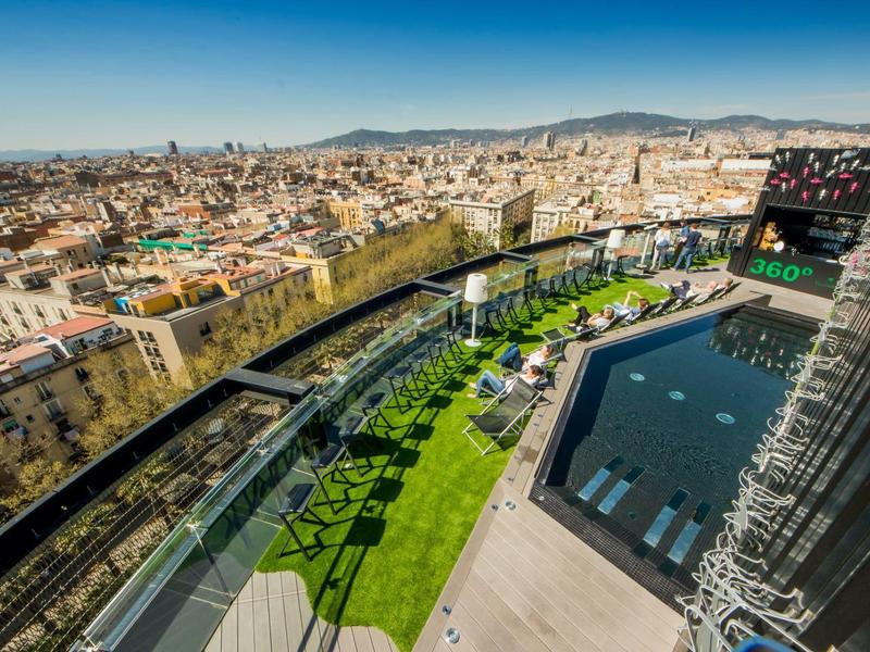 Blick über eine Stadt mit moderner Dachterrasse, grünem Rasen und Schwimmbecken unter blauem Himmel.