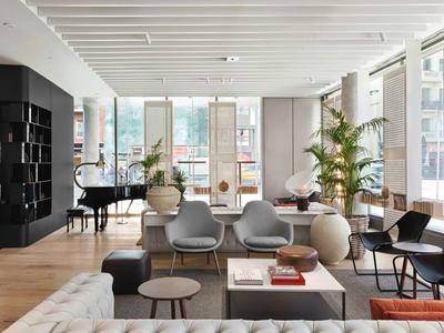 Un salotto d'hotel moderno con poltrone grigie, tavolini, piante e pianoforte a coda nero.