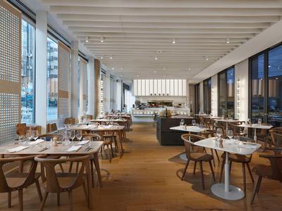 Modernes Restaurant mit Holzmöbeln, weißen Wänden und großen Fenstern mit Aussicht.