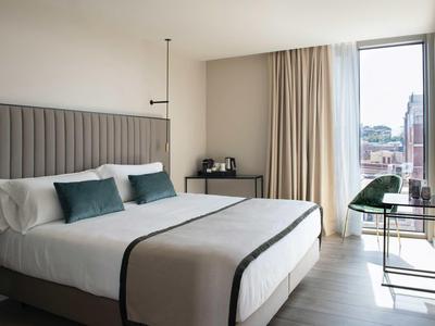 Modernes Hotelzimmer mit großem Bett, Schreibtisch und Fenster mit Blick auf die Stadt.