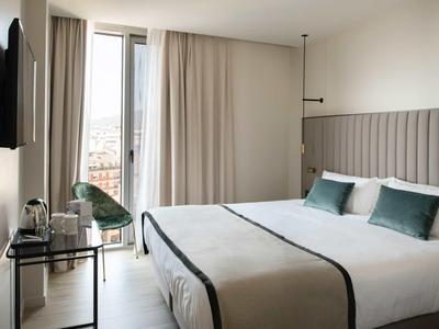 Modernes Hotelzimmer mit Doppelbett, grauem Kopfteil und Balkon mit Vorhängen.