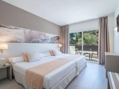 Moderní hotelový pokoj se dvěma jednolůžky, posezením a výhledem na terasu se zahradou.