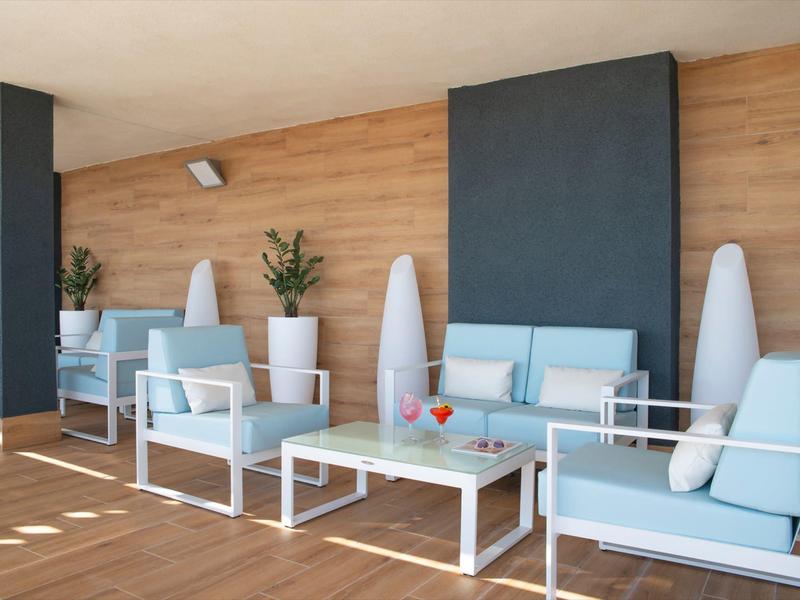 Moderní lounge s bílým nábytkem, modrými polštáři a dřevěnou zdí, ideální pro relaxaci.