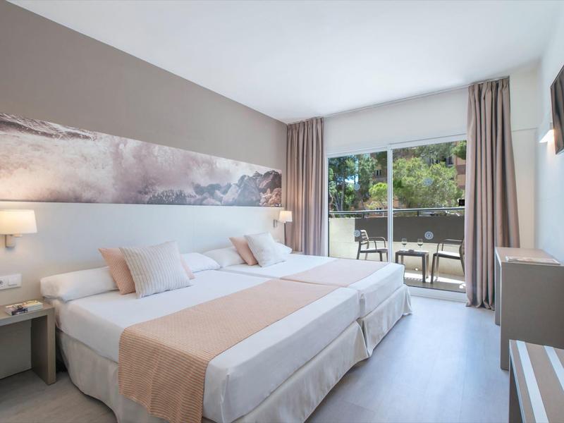 Moderní hotelový pokoj se dvěma jednolůžky, posezením a výhledem na terasu se zahradou.