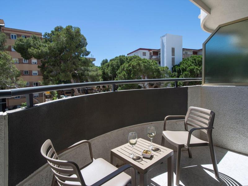 Balkon se dvěma židlemi a malým stolem, výhled na stromy a budovy za slunečného počasí