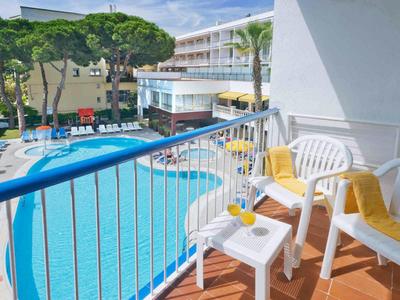 Balkon mit weißen Stühlen und Blick auf einen blauen Pool in einem Hotel mit Sonnenschirmen.