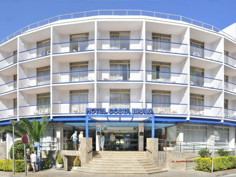 Mehrstöckiges, weißes Gebäude mit vielen Balkonen, bewachsen von Bäumen, bei strahlend blauem Himmel.