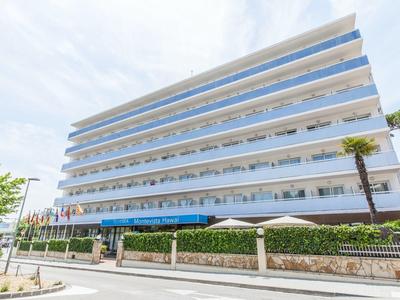 Nowoczesny budynek hotelu z wieloma balkonami i niebieskimi markizami pod zachmurzonym niebem.