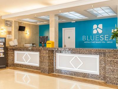 Moderner Hotel-Check-in mit blauem Logo, hellen Wänden und beleuchtetem Empfangstresen aus Stein.