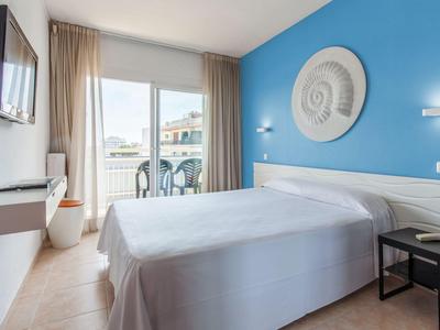 Licht hotelkamer met tweepersoonsbed, balkon en blauwe geschilderde muur.