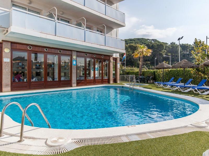 Basen hotelowy z leżakami i szklanymi balkonami w słoneczny dzień.