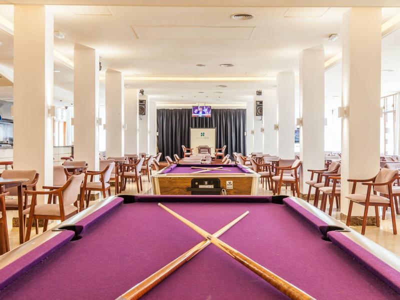 Wnętrze z kilkoma fioletowymi stołami bilardowymi i rzędami krzeseł w jasnym pomieszczeniu.