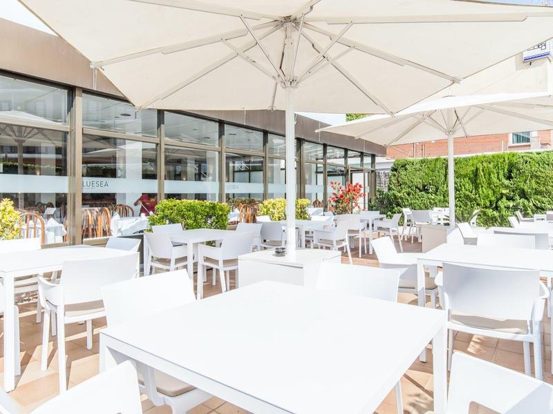 Jasna, nowoczesna restauracja na zewnątrz z białymi stołami, krzesłami i dużymi parasolami.