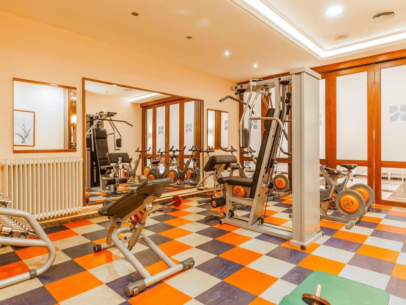 Jasna siłownia z kolorową podłogą i różnym sprzętem do ćwiczeń.