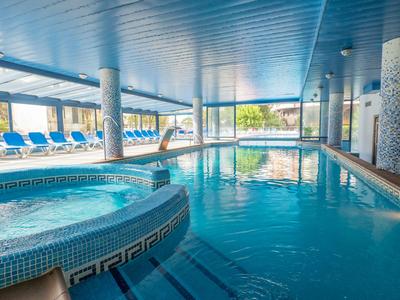 Overdekt gebied met verwarmd zwembad en jacuzzi, blauwe ligstoelen op de achtergrond.