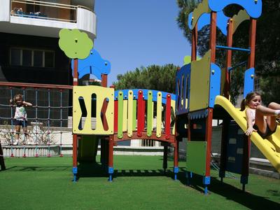 Bunter Spielplatz mit Rutsche, Klettergerüst und Netzanlage auf grünem Kunstrasen.