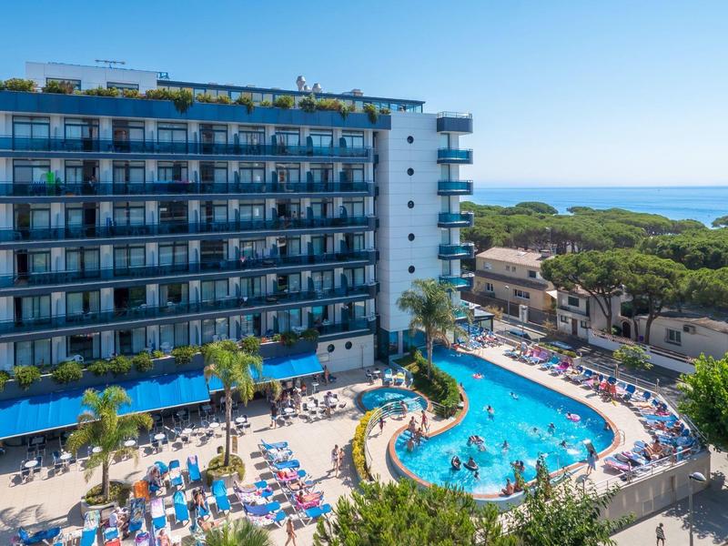Mehrstöckiges Hotel mit Balkonzimmern, großem Pool, Sonnenschirmen und Blick auf das Meer.