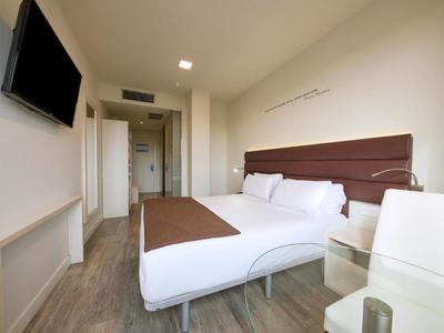 Camera d'hotel moderna con letto matrimoniale, TV a schermo piatto e pavimento in legno chiaro.