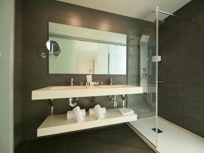 Bagno moderno con grande specchio, doppio lavabo e doccia a filo pavimento.