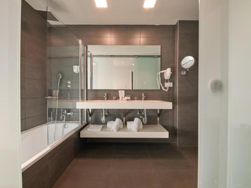 Modernes Badezimmer mit braun-weißen Fliesen, Badewanne, großem Spiegel und Doppelwaschbecken.