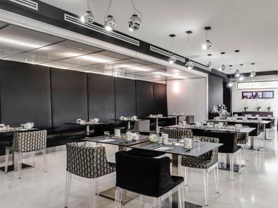 Modernes Hotelrestaurant mit schwarzen Tischen, gemusterten Stühlen und deckenmontierten Lampen.