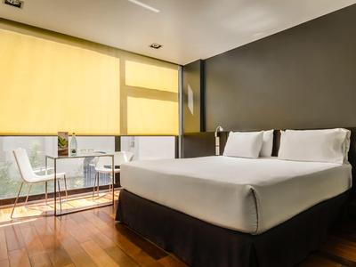 Modern hotel room with large bed, wooden floor, and balcony with seating.