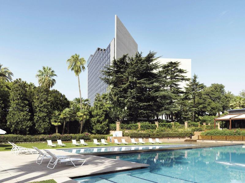 Modern hotel pool area with loungers and palm trees under clear sky