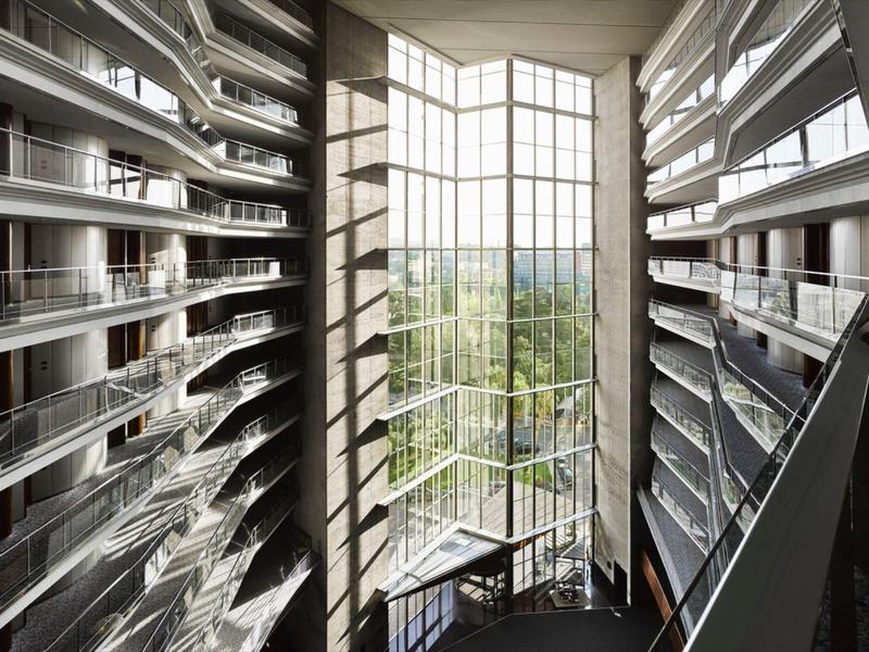 Modern hotel interior with large windows and balconies, light casting shadows on the floor.