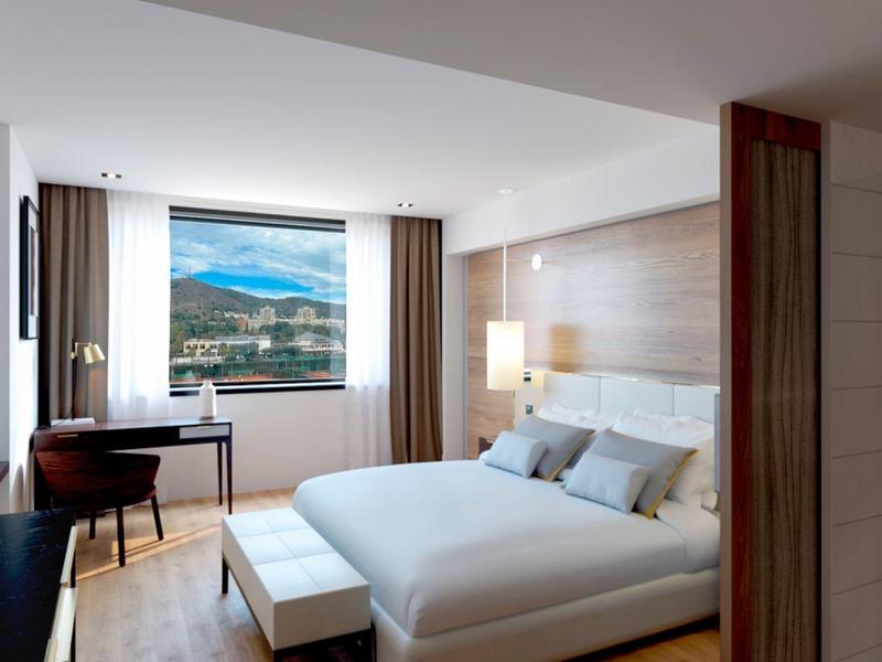 Modern hotel room with a small desk, comfortable bed, and mountain view through the window.