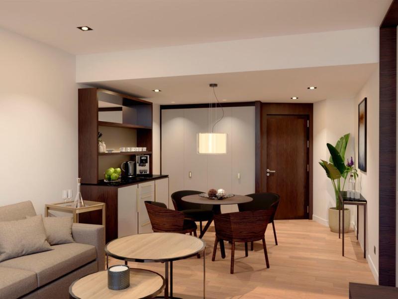 Modern furnished hotel apartment with seating area, dining table, and kitchenette.