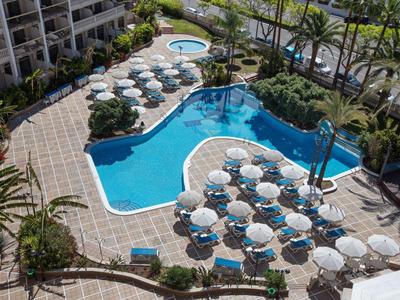 Piscina dell'hotel con ombrelloni bianchi rotondi, circondata da palme e da un edificio a più piani.