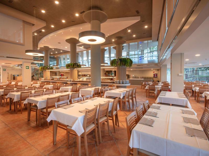 Prostorná moderní jídelna s bílými ubrusy a dřevěným nábytkem v jasném prostředí.