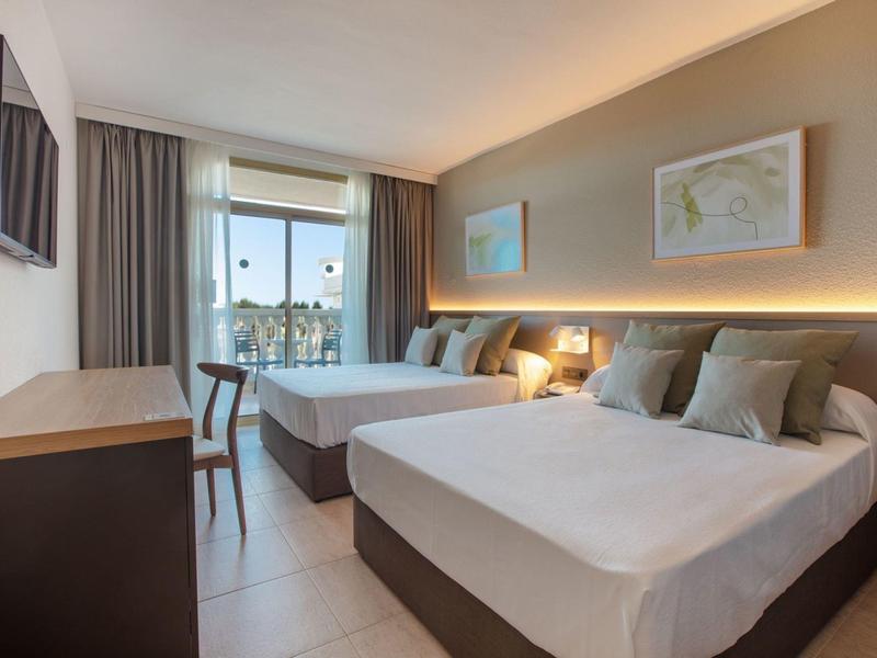 Světle hotelový pokoj se dvěma postelemi, pracovním stolem, židlí a velkým oknem se záclonami.