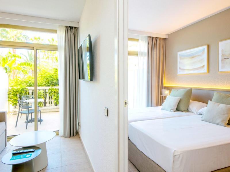 Světý hotelový pokoj s manželskou postelí, moderním zařízením a balkonem s výhledem do zeleně.