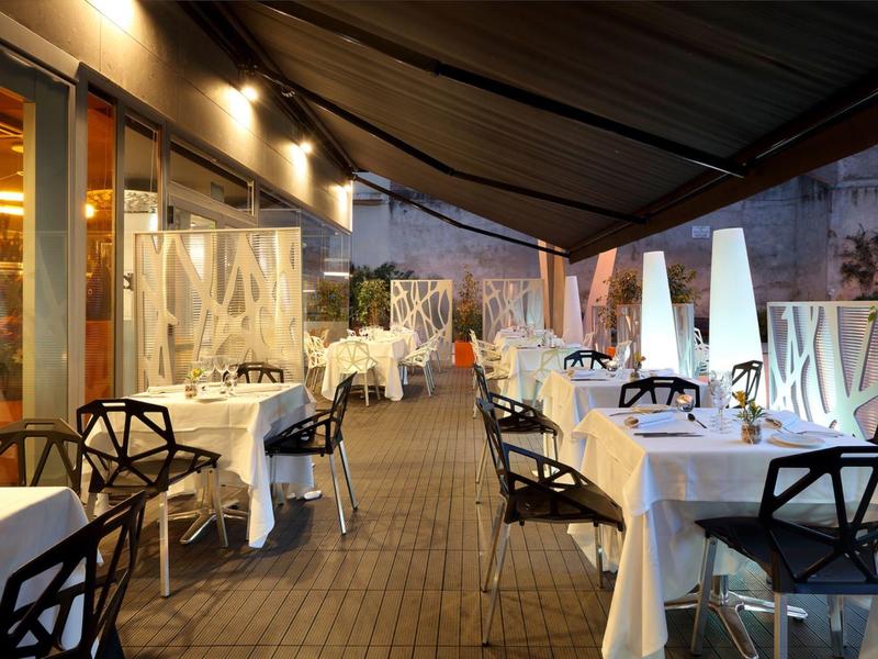 Evening restaurant terrace with set tables and modern chairs under a canopy.