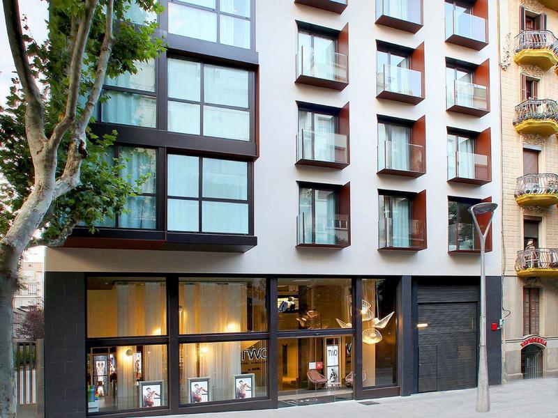 Facade of a hotel with large windows and a tree in front on a city street.