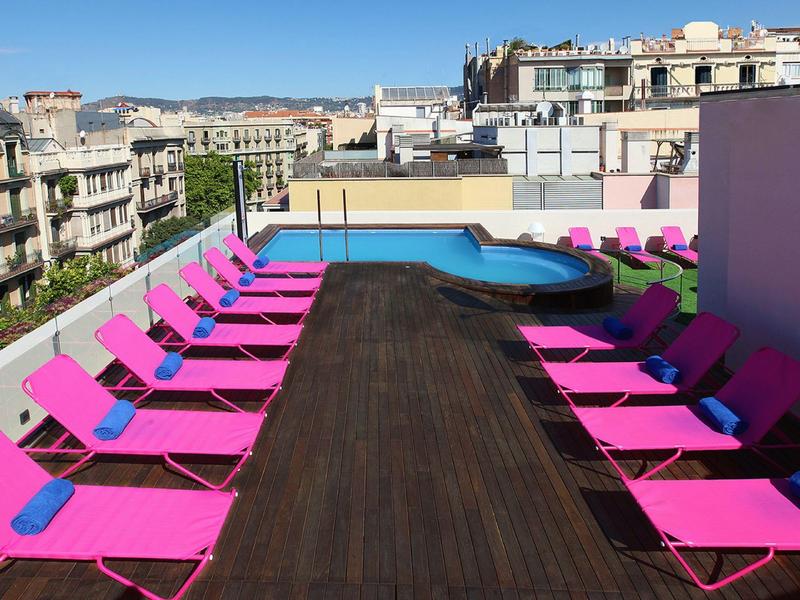 Rooftop terrace with pink lounge chairs and small pool in urban setting.