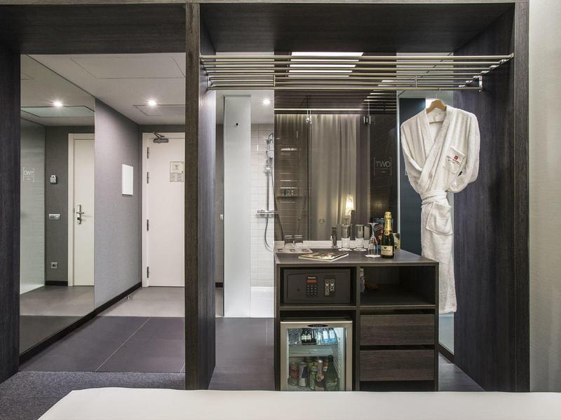 Modern hotel room area with minibar, bathrobe, and lighting.