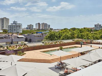 Große Dachterrasse mit Pool, Sonnenliegen und Sonnenschirmen, umgeben von Stadtgebäuden.