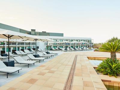 Moderne hotelzwembad met ligstoelen en parasols naast een meerlagig hotelgebouw.