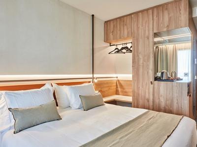 Camera d'hotel moderna con letto matrimoniale, legno chiaro e atmosfera accogliente.