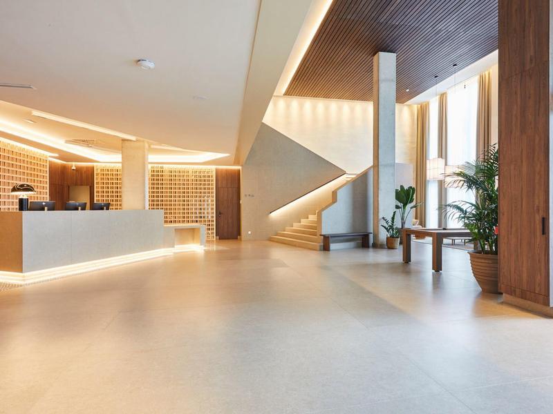 Ingresso di hotel moderno con bancone illuminato e scala in legno minimalista.