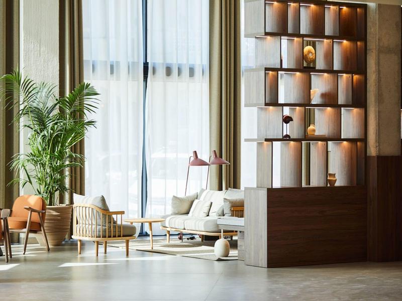 Sala luminosa dell'hotel con poltrone, divano, tavolino e grande pianta verde.