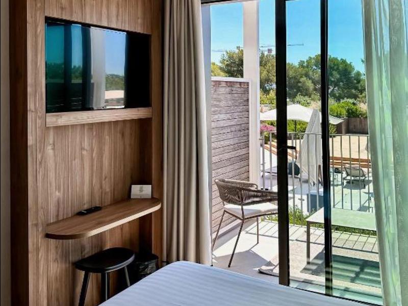 Camera d'hotel moderna con letto bianco, TV a muro e terrazza con mobili esterni.