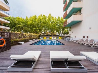 Hotelpool mit Holzterrasse, Liegestühlen und üppigen grünen Bäumen im Hintergrund.